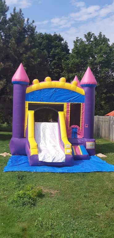 Colorful inflatable bounce house with a slide in a backyard.