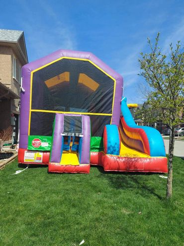 Colorful inflatable bounce house with slide set up on a grassy lawn on a sunny day.