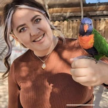 Woman smiling while holding a colorful parrot on her hand.