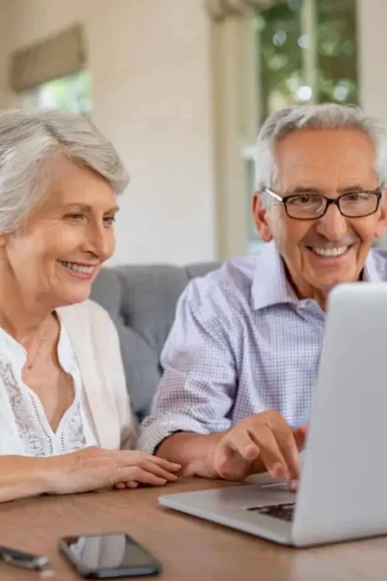 Elderly couple smiling while using a laptop.