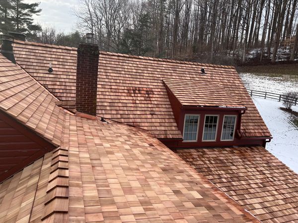 A new cedar shingle roof on a house with a dormer and chimney in winter.