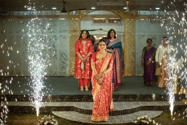 Women in traditional attire walking amidst festive sparkler fireworks.
