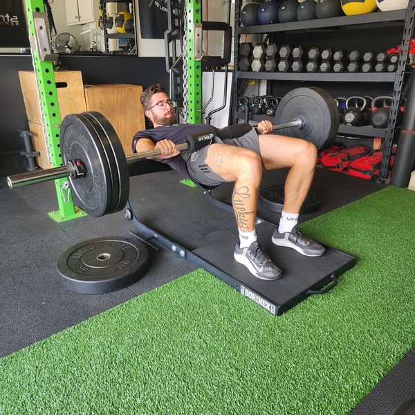 Man performing barbell hip thrust exercise in a gym.