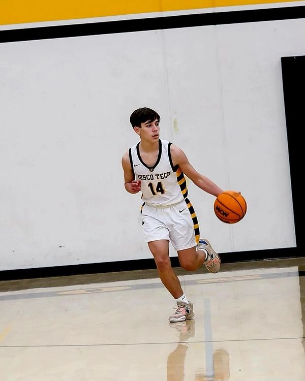 Young basketball player in white uniform dribbling the ball on court.