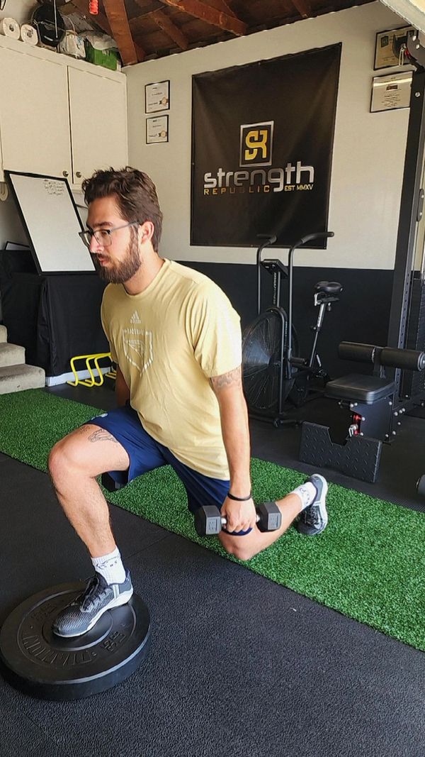 Man performing weighted Bulgarian split squat in a gym.