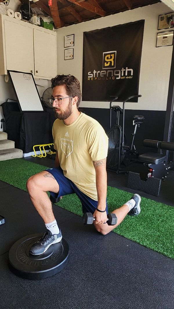 Man performing a weighted lunge exercise in a gym.
