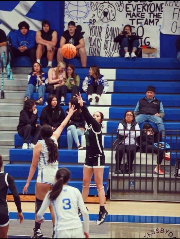 Female basketball player shooting over defender during a game in a crowded gym.