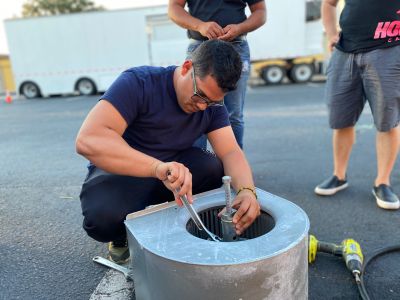 A man uses tools to fix or assemble equipment outdoors on asphalt.