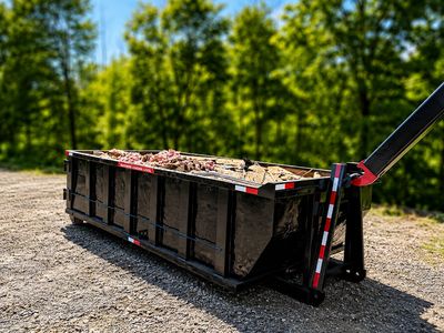 Large black dumpster filled with debris on a gravel surface.