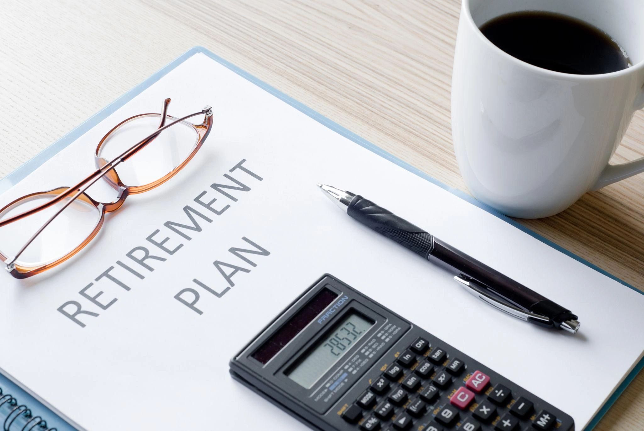 Retirement plan document with glasses, pen, calculator, and coffee cup on desk.