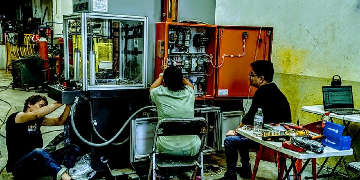 Three people work on repairing and troubleshooting industrial electrical equipment.