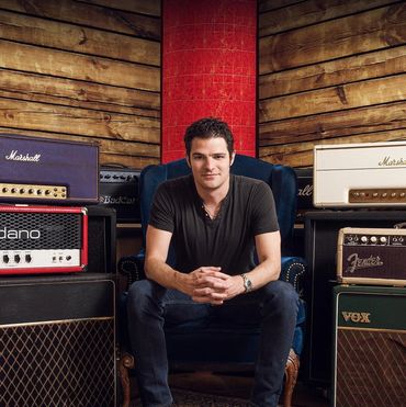 Man sitting between guitar amplifiers.