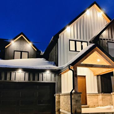 Modern house illuminated at night with snow on the roof.