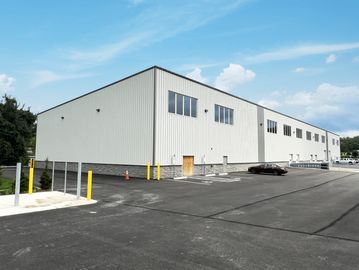 Large white industrial warehouse with ample parking space under a clear sky.