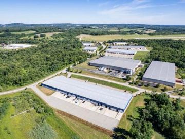 Aerial view of industrial warehouses surrounded by greenery under a clear sky.