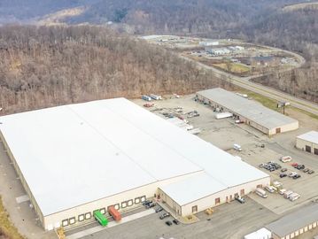 A large industrial warehouse surrounded by vehicles and trees.