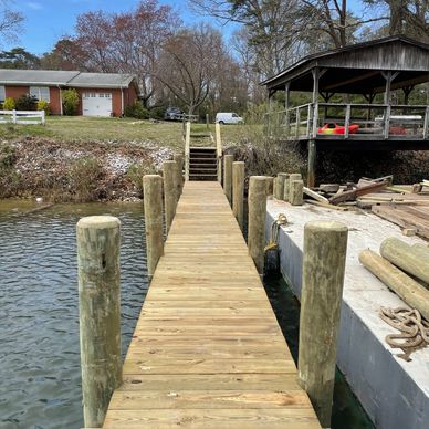 A wooden dock extends over calm water towards a house and gazebo.