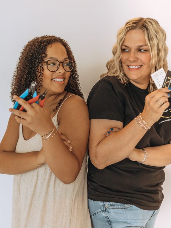 Two women smiling and looking at each other, holding tools and cards.