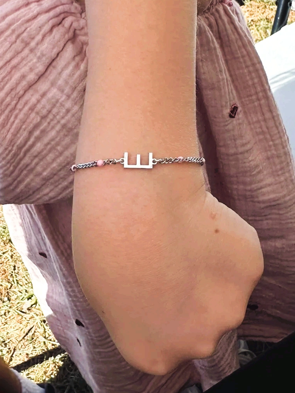 Child showing a wrist bracelet with an initial.