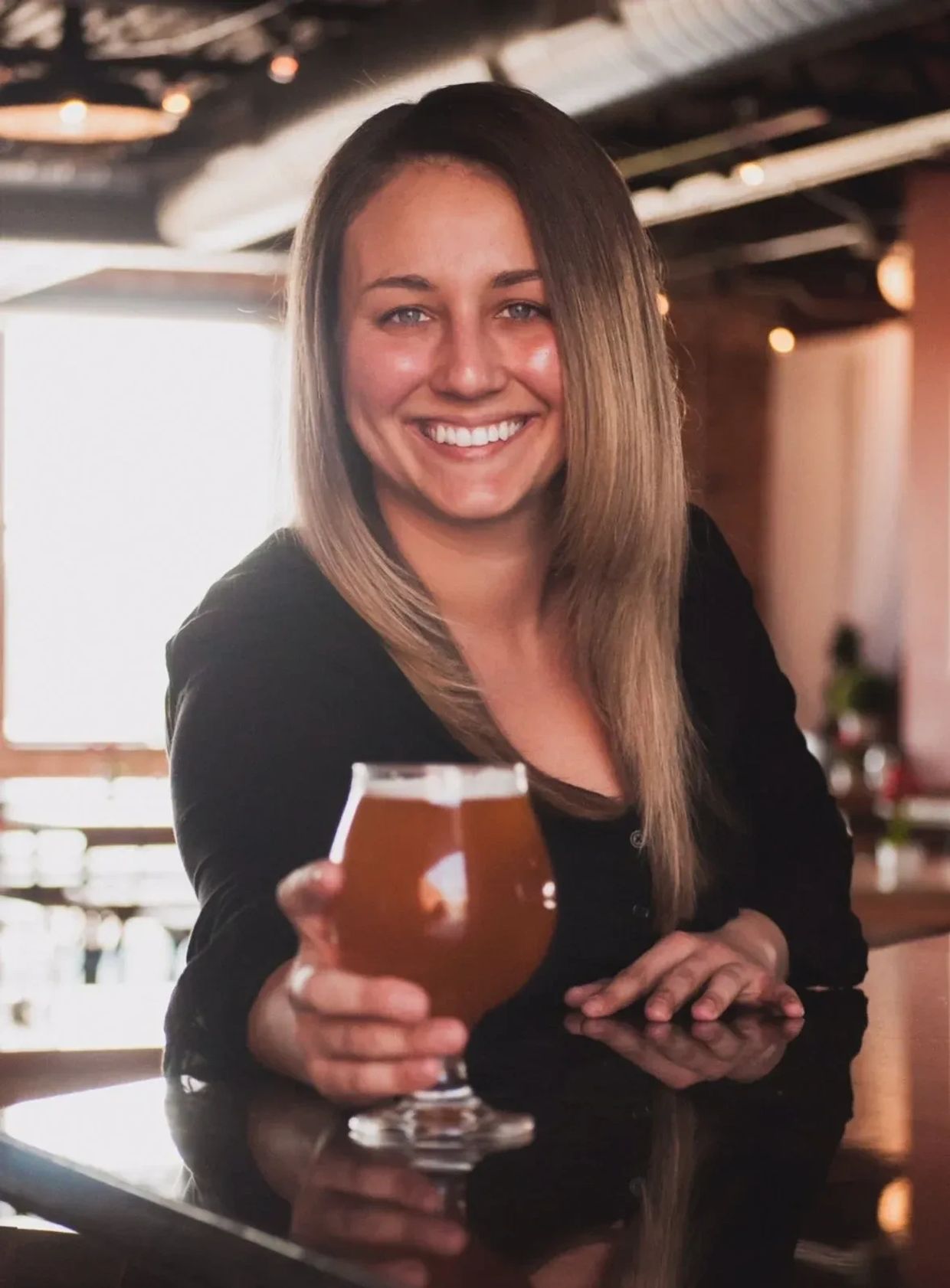 Smiling woman holding a glass of beer in a cozy setting.