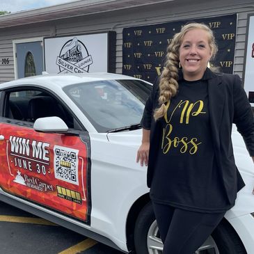 A man and woman stand by a car with a promotional sign for a June 30th contest.