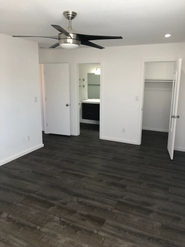 Empty modern bedroom with dark wood flooring and ceiling fan.