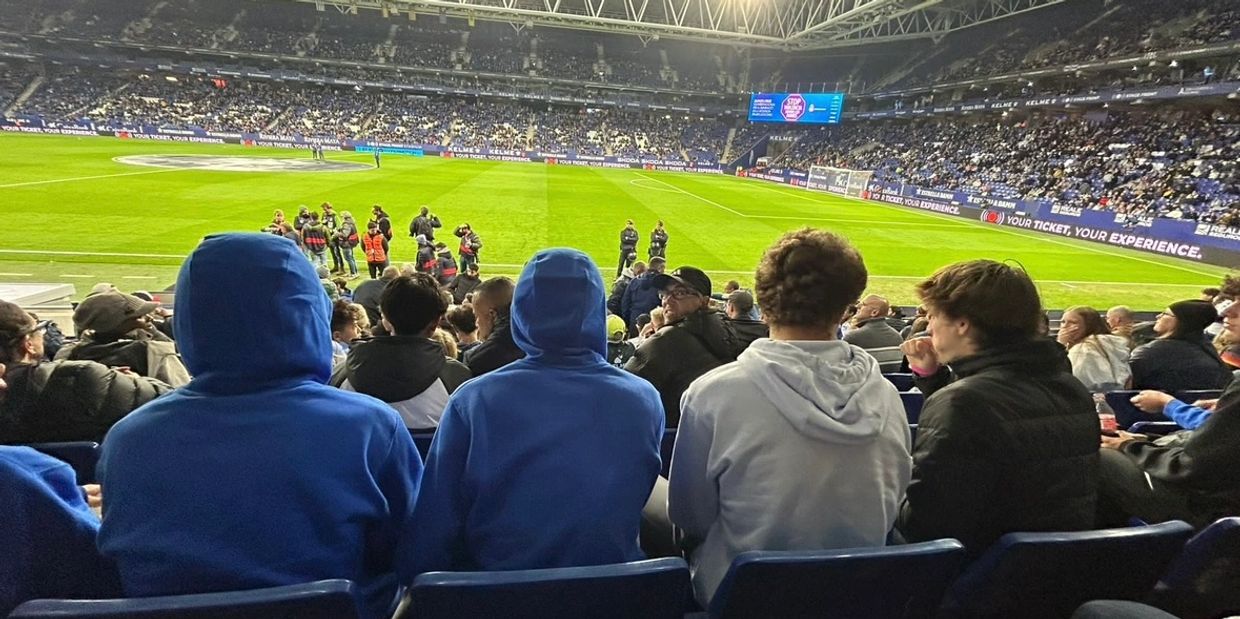 Fans watch a soccer match in a large stadium under bright lights.