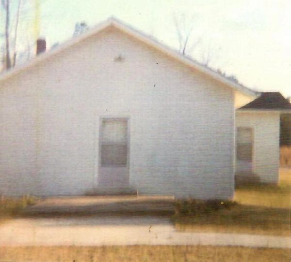 Old white wooden house with a single window and door.