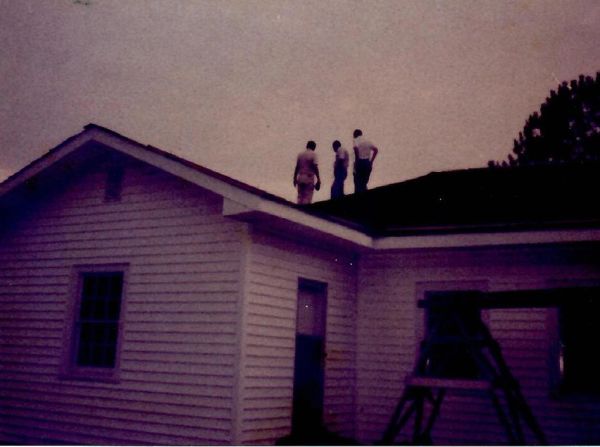 Three people standing on the roof of a house at dusk.