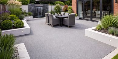 Modern backyard patio with gray seating, waterfall feature, and lush greenery.