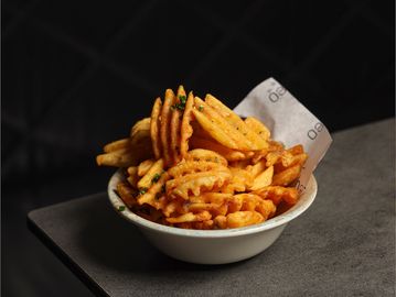 A bowl of seasoned waffle fries on a dark surface.