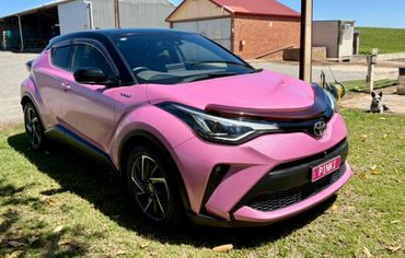 Pink Toyota car with a black roof parked on grass.