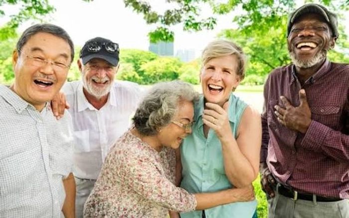 A diverse group of elderly friends laughing together outdoors.