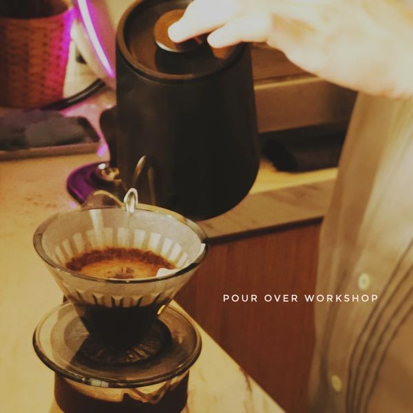 Hand pouring water over coffee grounds in a pour-over workshop.