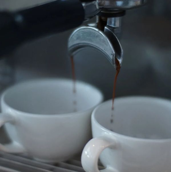 Espresso pouring into two white cups from a coffee machine.