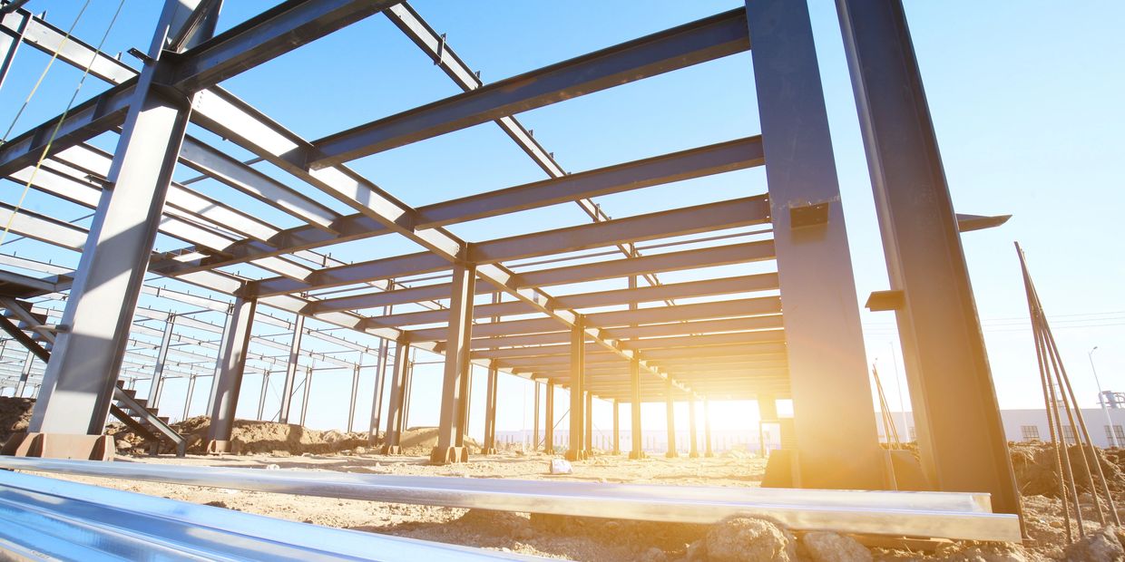Steel framework of a building under construction with sunlight streaming through.