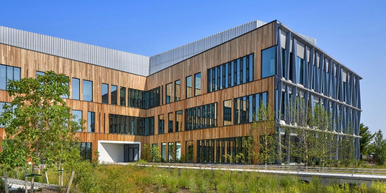 Modern office building with wooden and glass facade under clear blue sky.