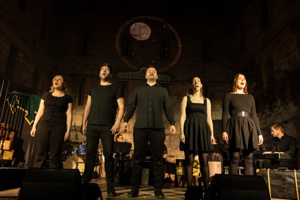 A group of five people singing on stage during a performance.