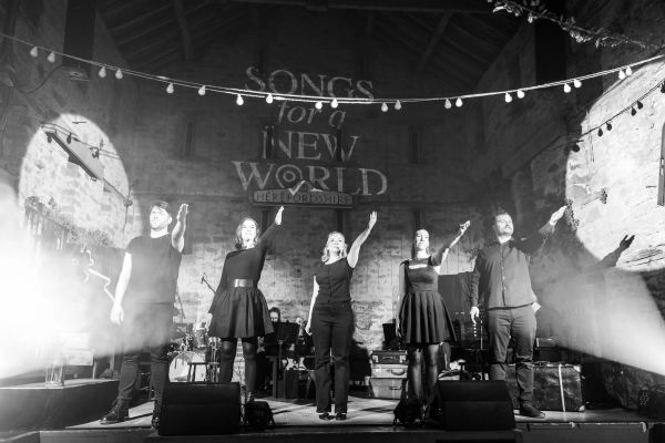 Five performers on stage gesturing with raised hands.