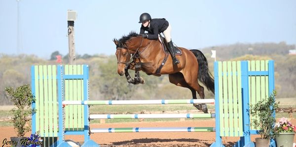 Horse and rider jump a colorful obstacle in a show jumping event.