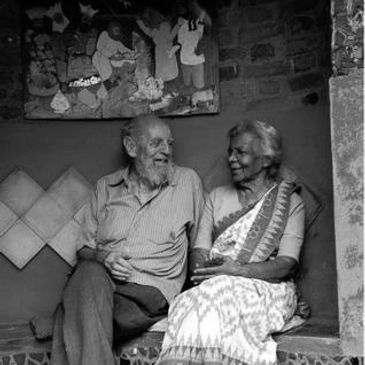 Elderly couple sharing a joyful moment on a bench against a brick wall.