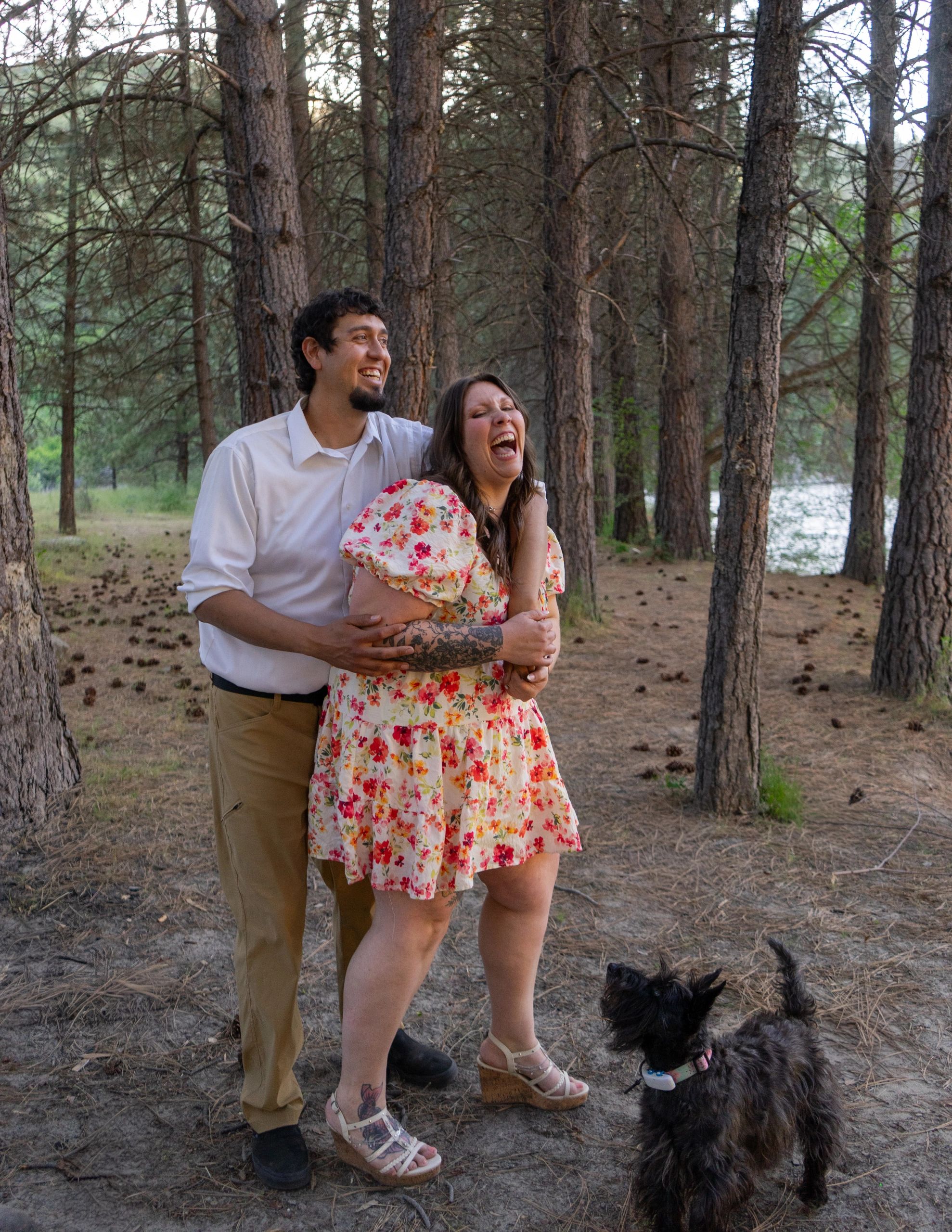 Happy couple laughing together in a forest with their dog.