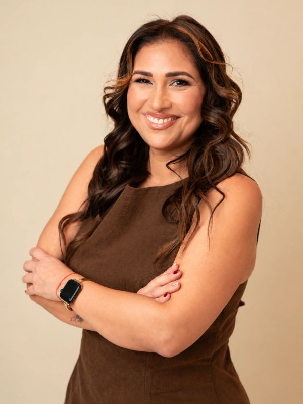 Smiling woman with crossed arms wearing a brown dress.