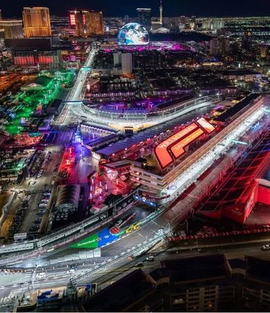 Night view of a lit-up racetrack and cityscape.