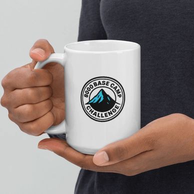 Person holding a white mug with an 8000 Base Camp Challenge logo.
