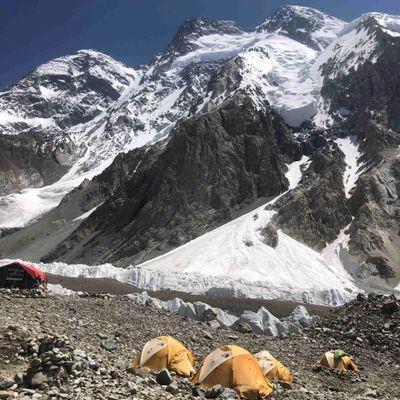 Yellow tents set up at a snowy mountain base camp beneath towering peaks.