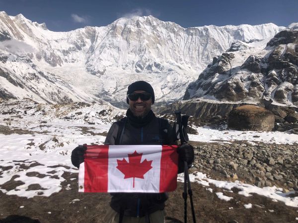 Man holding Canadian flag in snowy mountain landscape.