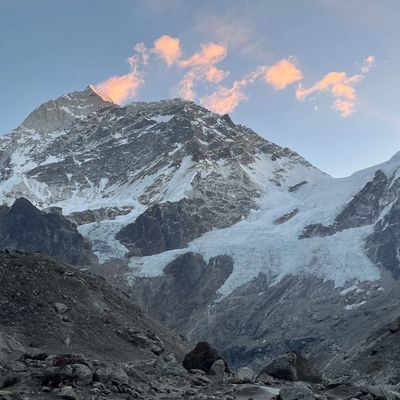 Sunset light touches snow-covered mountain peaks with rocky foreground.