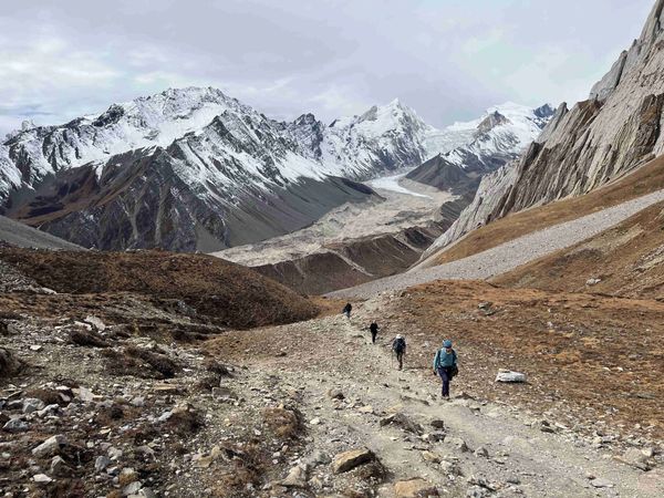 Hikers trekking on a rugged mountain path with snowy peaks in the background.