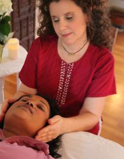 A woman gently massages another woman's head in a calm setting.